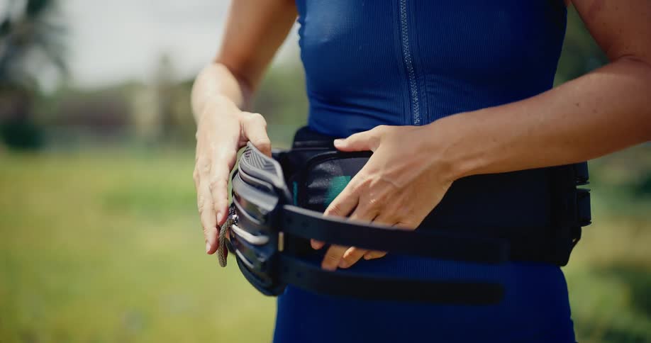 Slow motion closeup of a woman's hands securing a kitesurfing harness around her waist