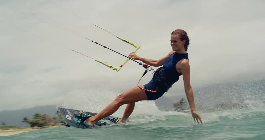 Smiling woman gracefully kitesurfs across the ocean, gliding over the waves in beautiful slow motion