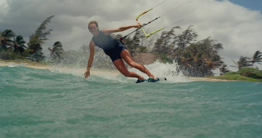 A female kitesurfer smiles while gliding towards the camera in slow motion on a beautiful tropical ocean