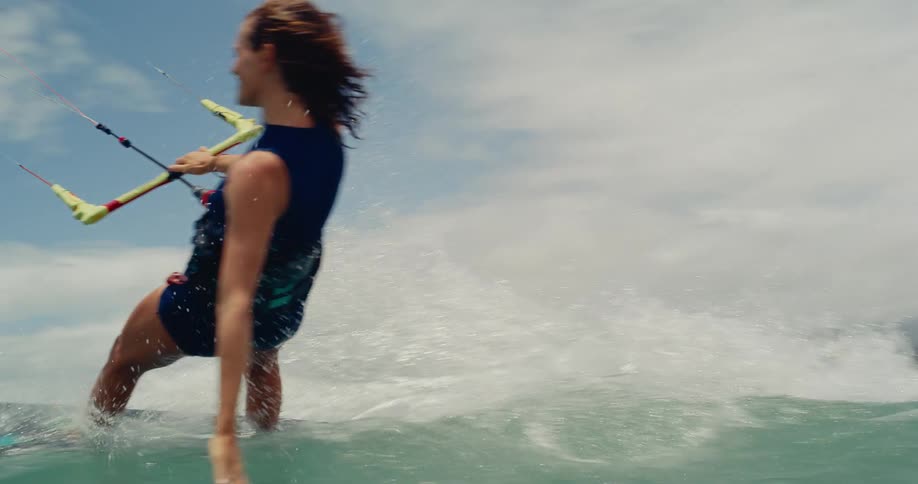 Low angle slow motion shot of a happy woman kitesurfing in the ocean on a beautiful day