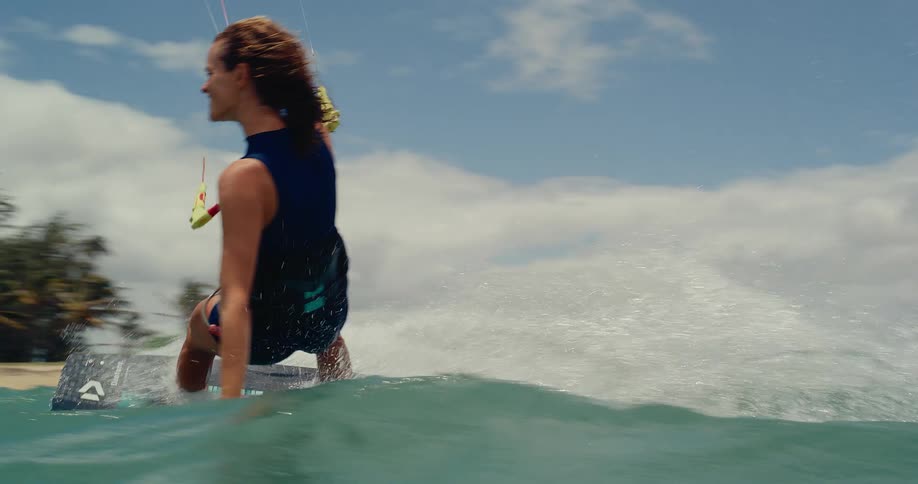 A smiling woman kitesurfs past the camera in slow motion on a beautiful tropical day