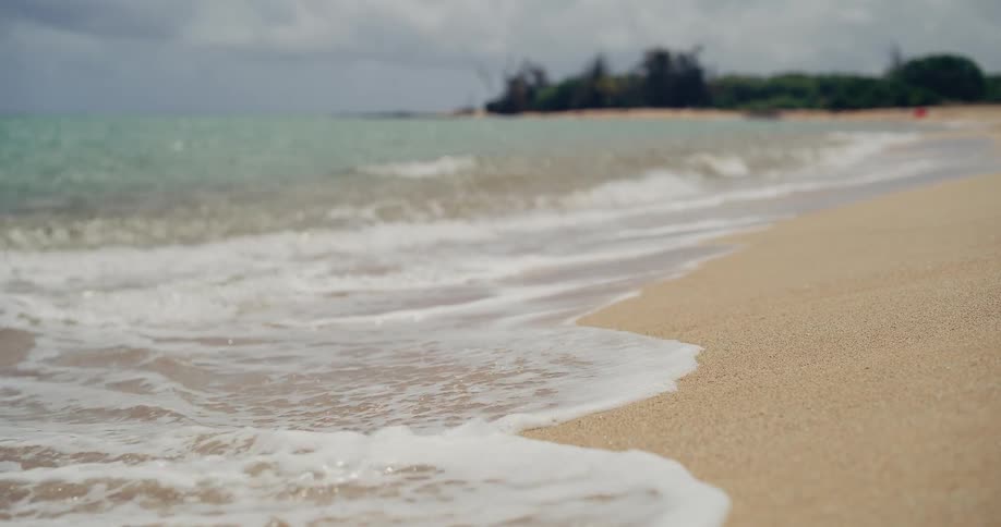 Calm sea foam from gentle waves slowly washes ashore on a beautiful sandy beach under a cloudy sky