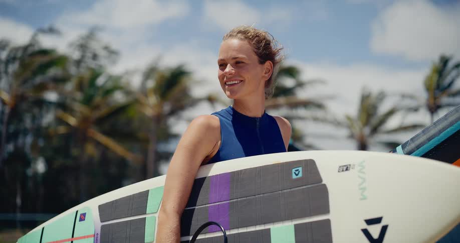 Portrait of a beautiful athletic young woman smiling with her kitesurfing gear on a sunny day, living a healthy and adventurous lifestyle