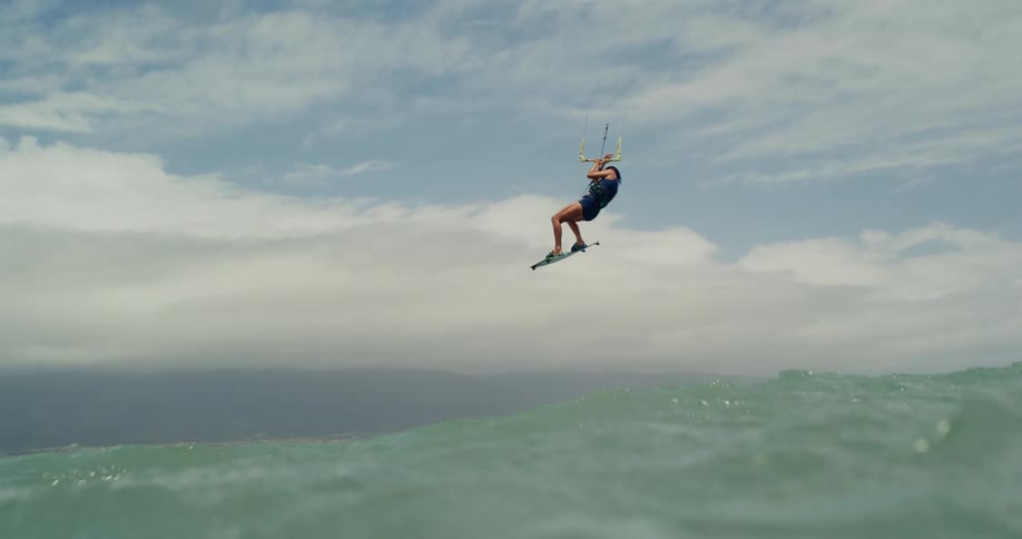 An amazing slow-motion shot of a female kitesurfer jumping high into the air over the ocean waves