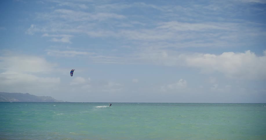 A kitesurfer glides across the serene turquoise ocean on a beautiful, breezy day
