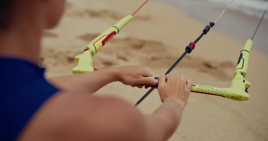 Close up over the shoulder shot of a person's hands preparing a kiteboarding control bar on a sandy beach