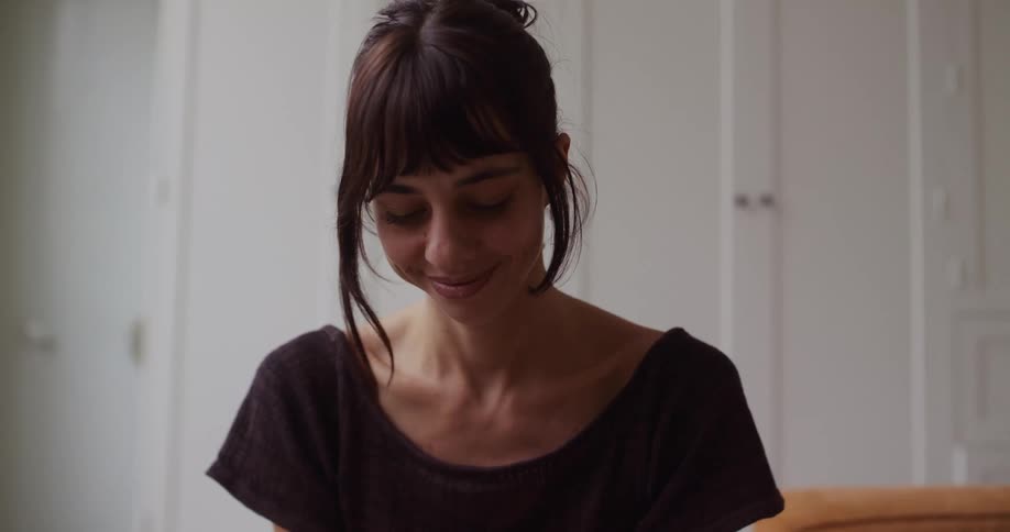 A thoughtful woman sits peacefully indoors, lost in a happy memory as a gentle smile crosses her face
