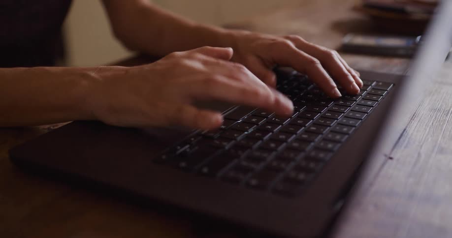 Close-up shot of a person's hands typing and navigating with the trackpad on a laptop resting on a wooden table