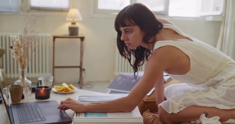 Side view of a focused woman in a white dress using her laptop on the coffee table in a cozy living room