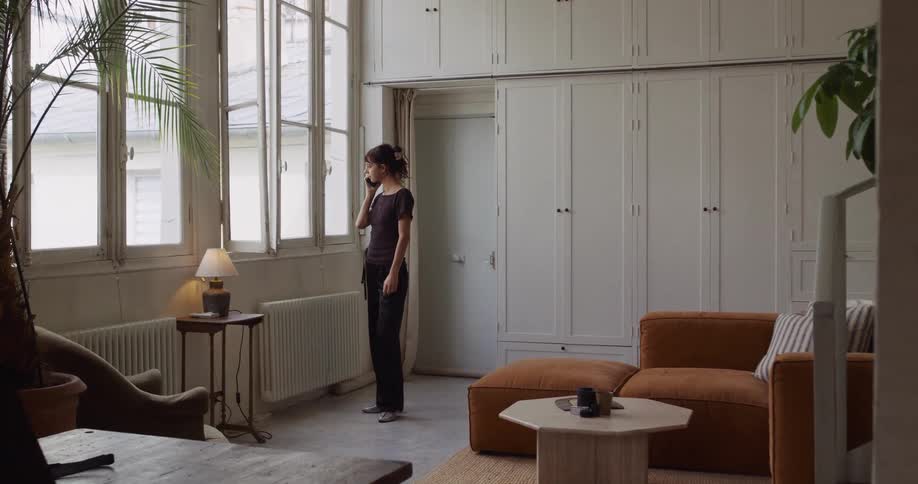 A young woman talks on the phone as she walks to the window in her spacious, naturally lit living room