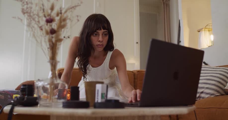 A focused woman works on her laptop, referencing a book in her cozy and stylish living room