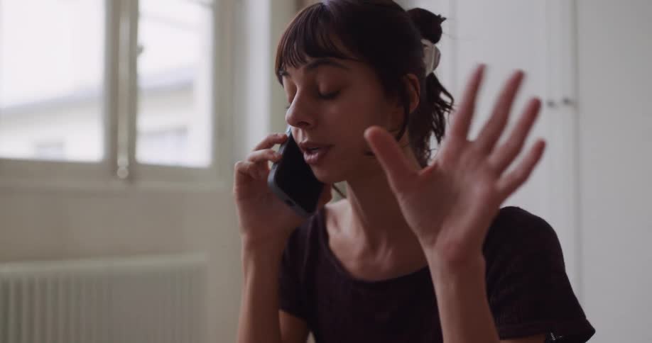 Slow-motion close-up of a young woman with dark hair talking on her phone and gesturing during a serious conversation indoors