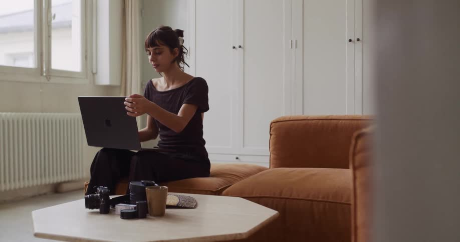 A female photographer finishes her work on a laptop in her modern living room, closes it, and takes a stretch break