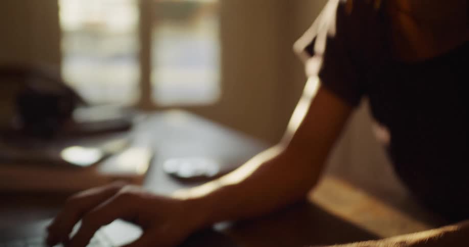 Cinematic slow-motion shot of a woman working on her laptop at home, illuminated by the warm glow of a nearby window