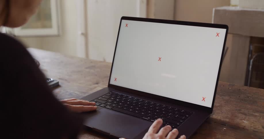 Over the shoulder shot of a person working on a laptop with a blank screen containing tracking markers for compositing
