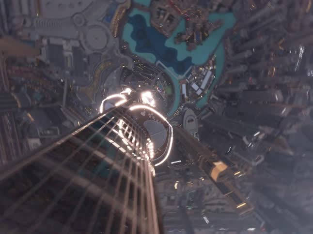 A dizzying first-person view looking straight down the side of the iconic Burj Khalifa as it descends towards the illuminated Dubai cityscape at dusk