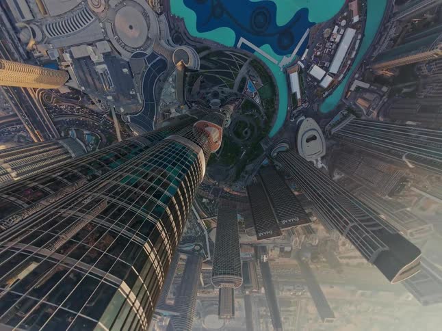 Dizzying 'little planet' effect aerial view rotates around a massive skyscraper, looking down over the Dubai cityscape and fountains