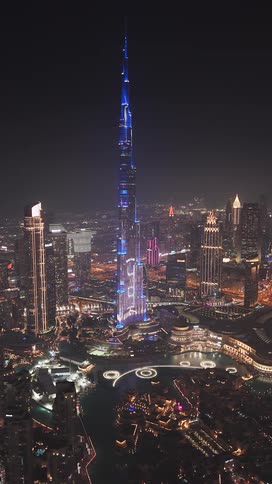 A stunning vertical aerial view of the Burj Khalifa illuminated with a blue light show against the vibrant Dubai cityscape at night