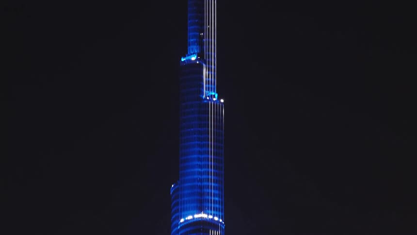 A dramatic tilt-up reveals the iconic Burj Khalifa skyscraper illuminated with striking blue lights against the dark night sky in Dubai