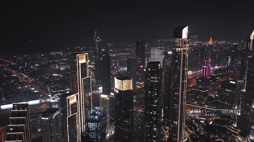 Stunning aerial shot of the dazzling Dubai skyline at night, featuring brightly lit, modern skyscrapers and sprawling city lights
