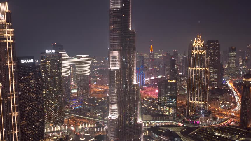 Stunning aerial shot tilting up the Burj Khalifa to reveal the futuristic Dubai skyline illuminated at night
