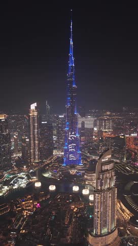 A stunning aerial view of the Burj Khalifa in Dubai displaying a vibrant blue light show against the night city skyline
