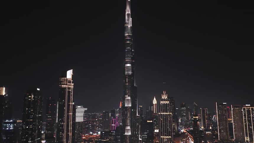 An aerial tilt-up shot reveals the magnificent Burj Khalifa towering over the illuminated Dubai cityscape at night