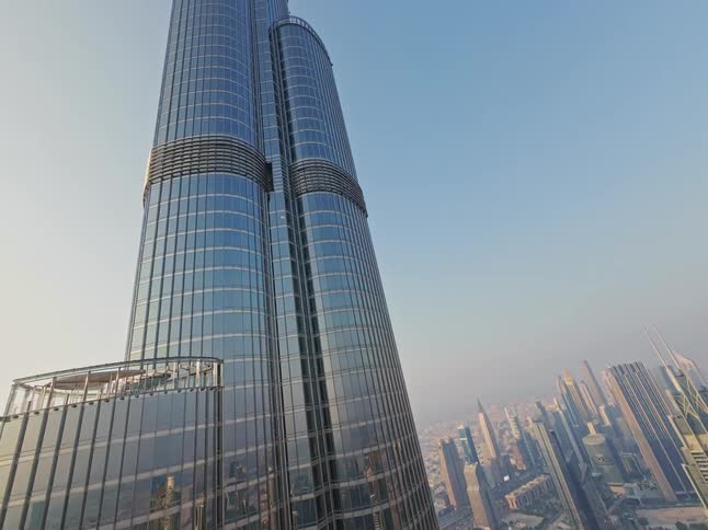 An impressive aerial view pans up the glass facade of the Burj Khalifa, revealing the vast modern cityscape of Dubai below