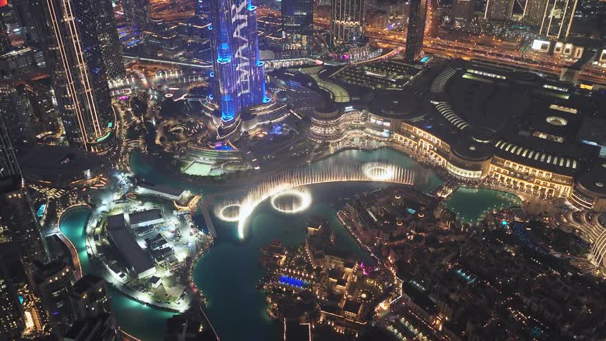 Stunning aerial view of the Dubai Fountain show and the illuminated Burj Khalifa at night, showcasing the vibrant cityscape