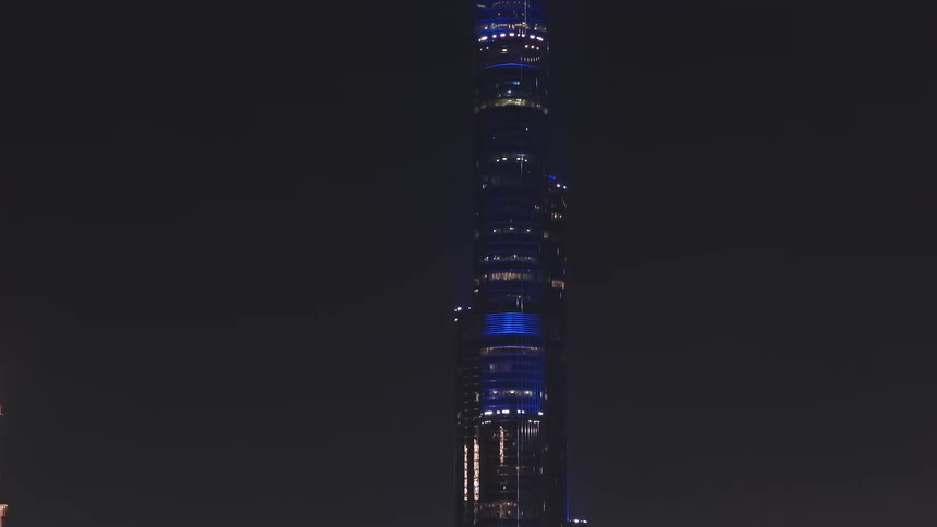 Slow tilt-up from a modern building to the iconic Burj Khalifa, brilliantly illuminated in blue against the dark night sky in Dubai