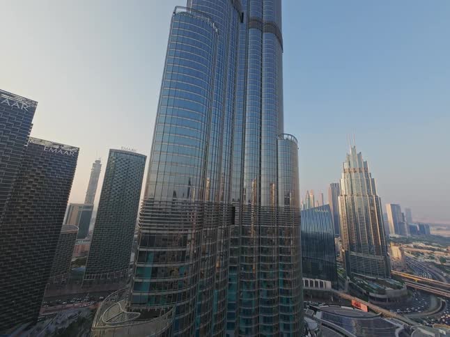 An aerial view slowly ascends the iconic Burj Khalifa, showcasing its reflective glass facade and the sprawling cityscape of Dubai at dusk
