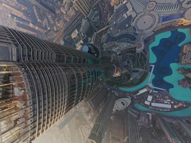 A mesmerizing top-down aerial shot slowly descends the side of the Burj Khalifa, revealing the vast cityscape of Dubai below