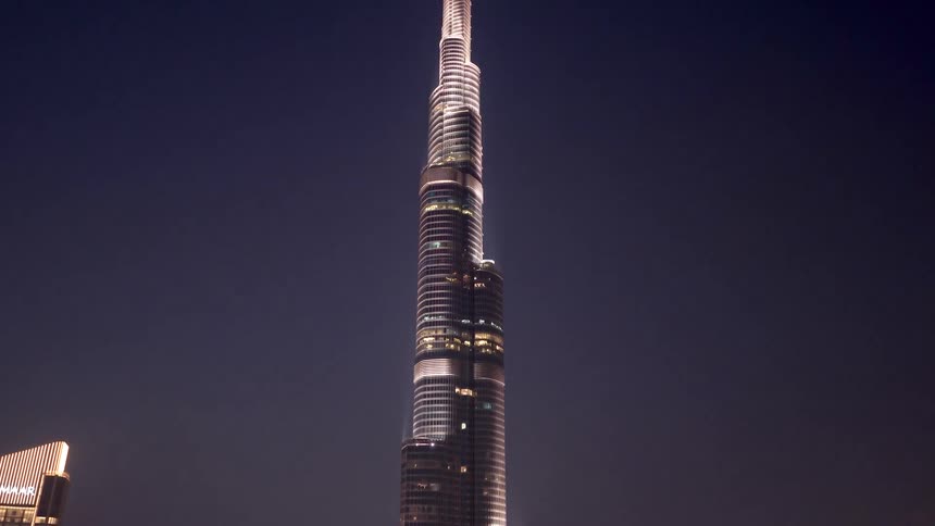 A slow and majestic tilt up shot of the illuminated Burj Khalifa skyscraper towering over the Dubai skyline at night