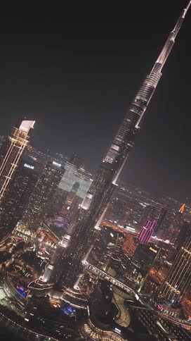 An aerial view pulls back from the illuminated Burj Khalifa, rotating to reveal the dazzling Dubai cityscape at night