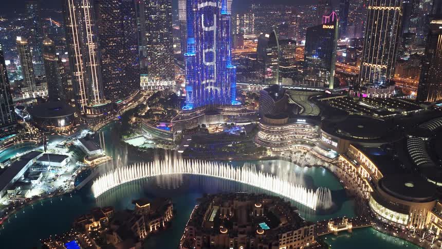 A dazzling high-angle view of the Dubai Fountain and Burj Khalifa light show at night, surrounded by the illuminated city skyline