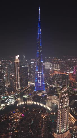 A stunning vertical aerial view of the Burj Khalifa at night, displaying a spectacular blue light show over the sparkling Dubai cityscape