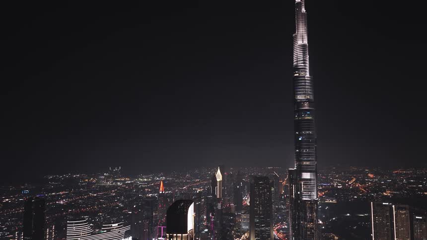 A stunning aerial view ascends over the vibrant Dubai cityscape at night, revealing the iconic Burj Khalifa towering into the dark sky