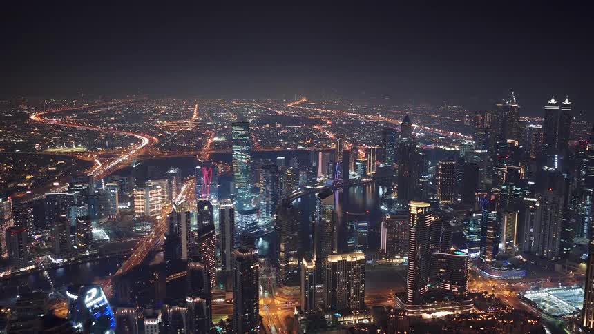 A spectacular aerial shot slowly pulls back to reveal the vast, brightly illuminated cityscape of a modern metropolis at night