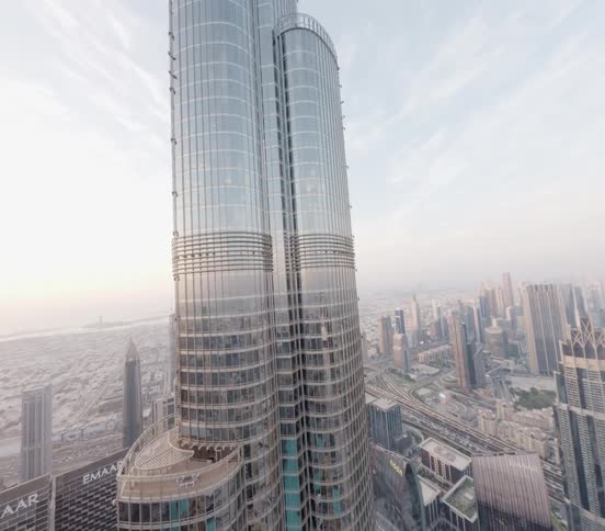 A breathtaking high-angle aerial view pans up the side of the iconic Burj Khalifa, showcasing the vast cityscape of Dubai below