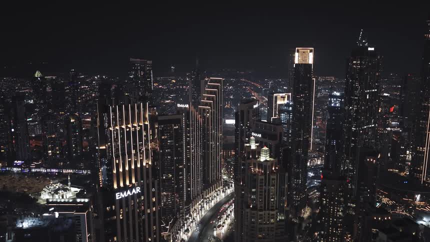 A slow aerial ascent reveals the glittering metropolis of Downtown Dubai, with its iconic skyscrapers and bustling streets illuminated against the night sky