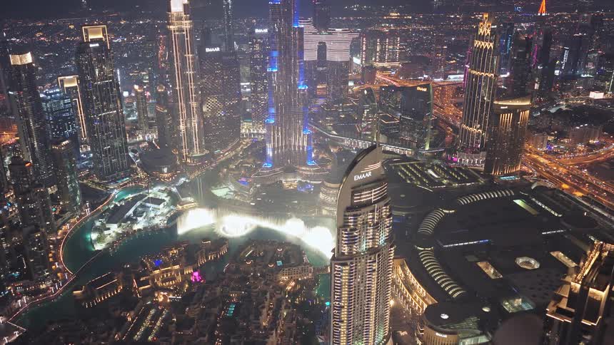A spectacular aerial view reveals the glowing Dubai downtown at night, showcasing the Burj Khalifa and the world's largest choreographed fountain system