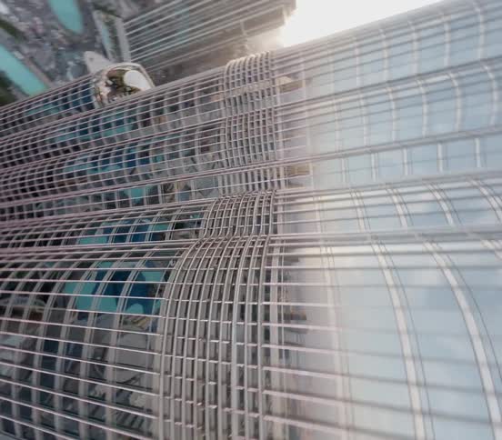 A breathtaking aerial shot tilts down the side of the Burj Khalifa, offering a dizzying top-down view of the Dubai cityscape below