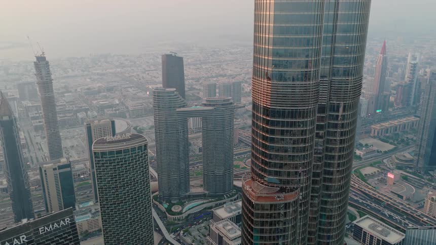 Epic aerial pull-back shot of the Burj Khalifa towering over the sprawling Dubai skyline and highways during a hazy sunset