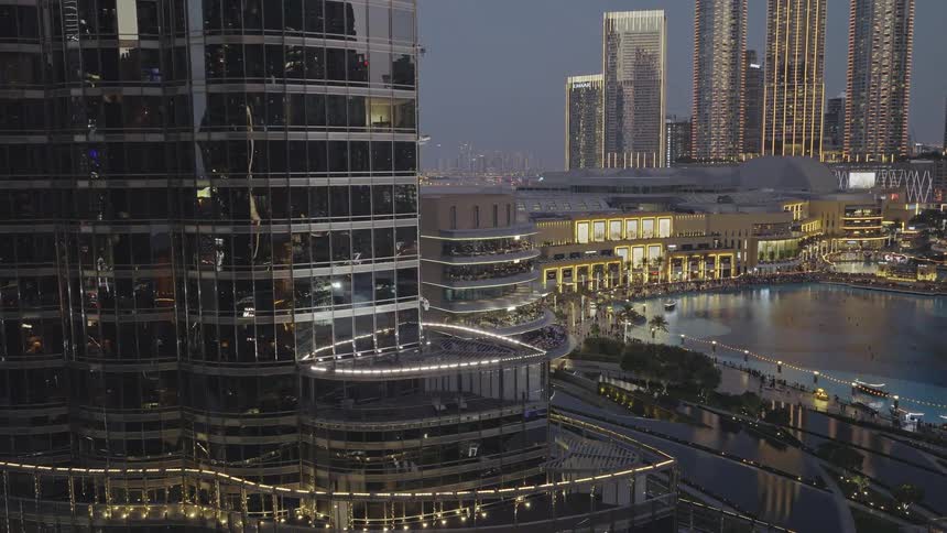 Slow aerial pan revealing the illuminated Dubai cityscape at dusk, showcasing the iconic Burj Khalifa and the bustling waterfront below