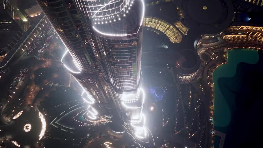 An incredible top-down aerial view slowly zooms out from the illuminated Burj Khalifa, revealing the vibrant Dubai cityscape at night