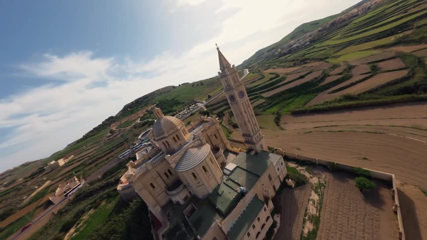 An FPV drone performs a cinematic orbit around the majestic Basilica of Ta' Pinu on the island of Gozo, showcasing its intricate architecture against the rural landscape