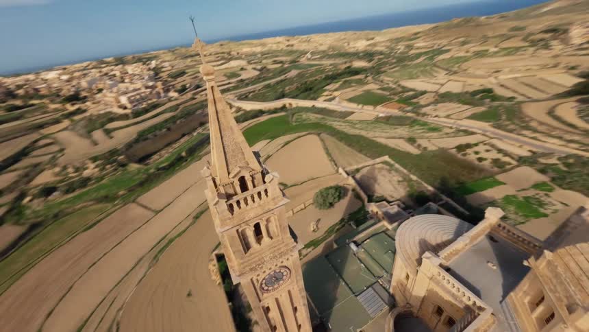 A cinematic FPV drone flight soars towards and up the majestic bell tower of the Ta' Pinu Basilica on the island of Gozo, Malta