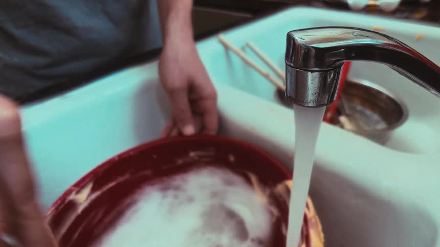 Close-up of a person scrubbing a soapy red bowl in a white kitchen sink with running water