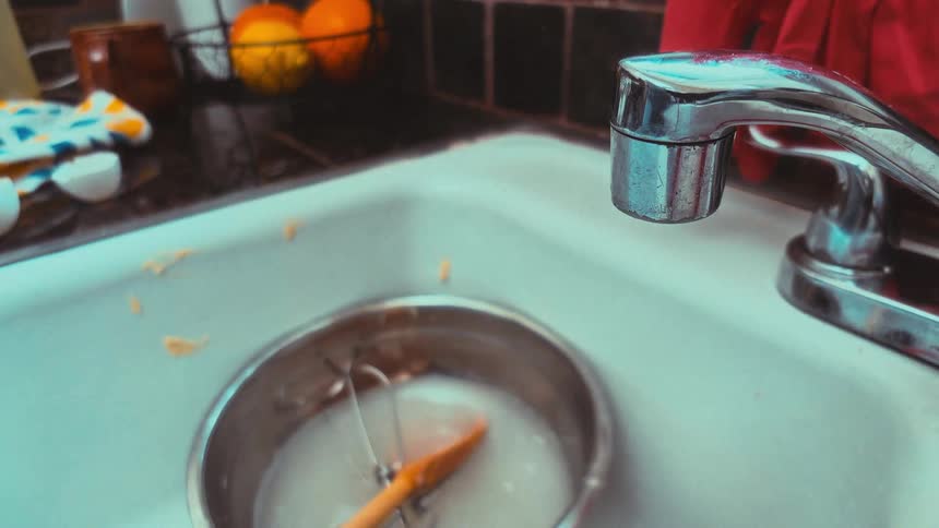 Close up of a person washing dirty baking utensils in a kitchen sink and turning off the running water