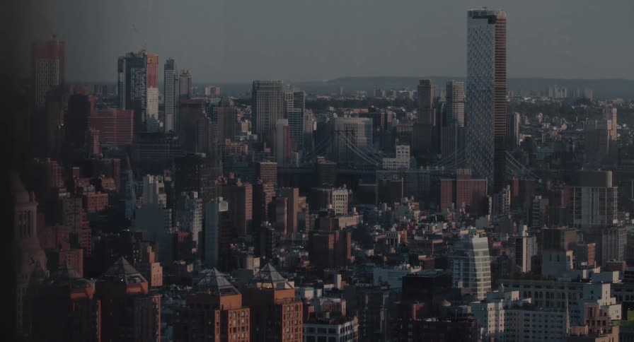 A static wide shot captures the Brooklyn skyline and a distant bridge under the warm glow of a hazy sunrise
